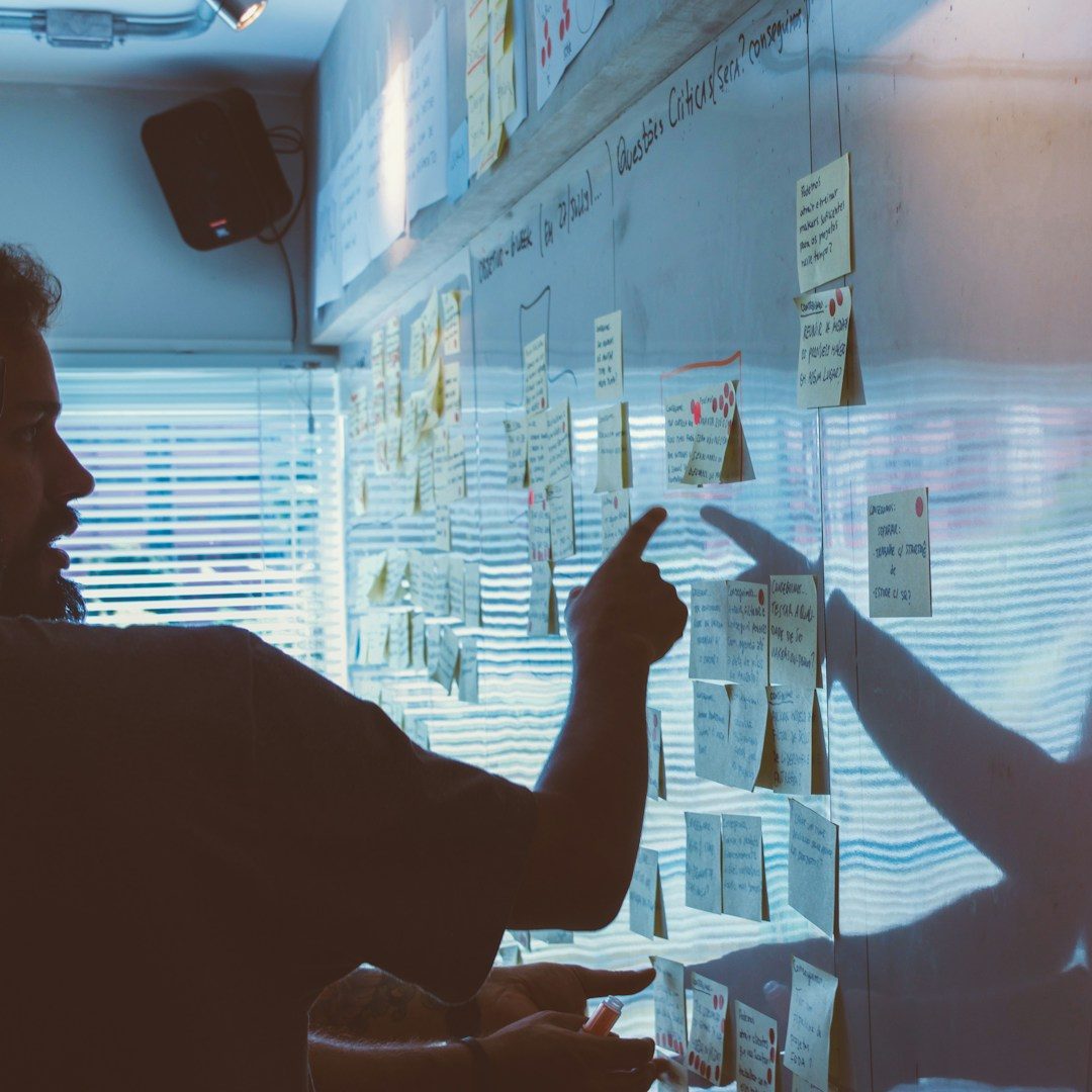 Ein Mann steht vor einem White Board mit Post-Its und zeigt auf eines dieser Post-Its.